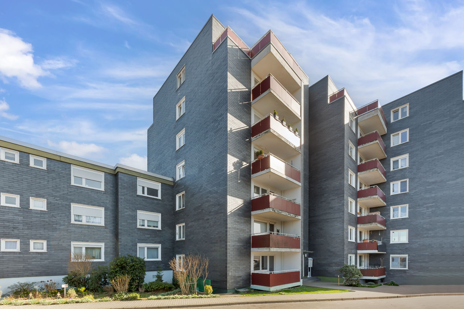 Mehrstöckiges Wohnhaus mit mehreren Balkonen und gepflegtem Vorgarten.