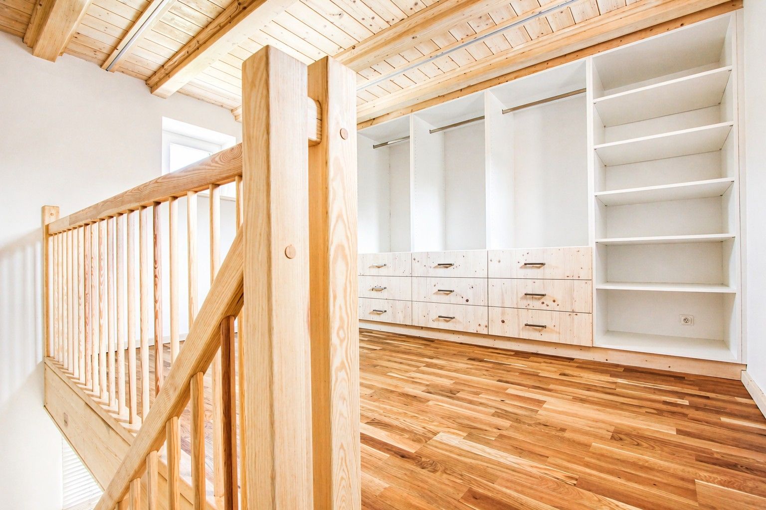 Heller Raum mit Holzgeländer, Holzdecke und offenem Einbauschrank mit Regalen und Schubladen.