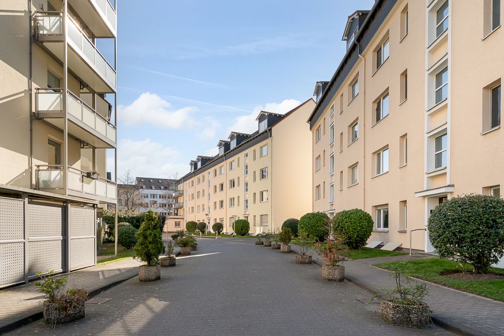Wohngebäude mit mehreren Etagen und bepflanzten Wegen dazwischen.