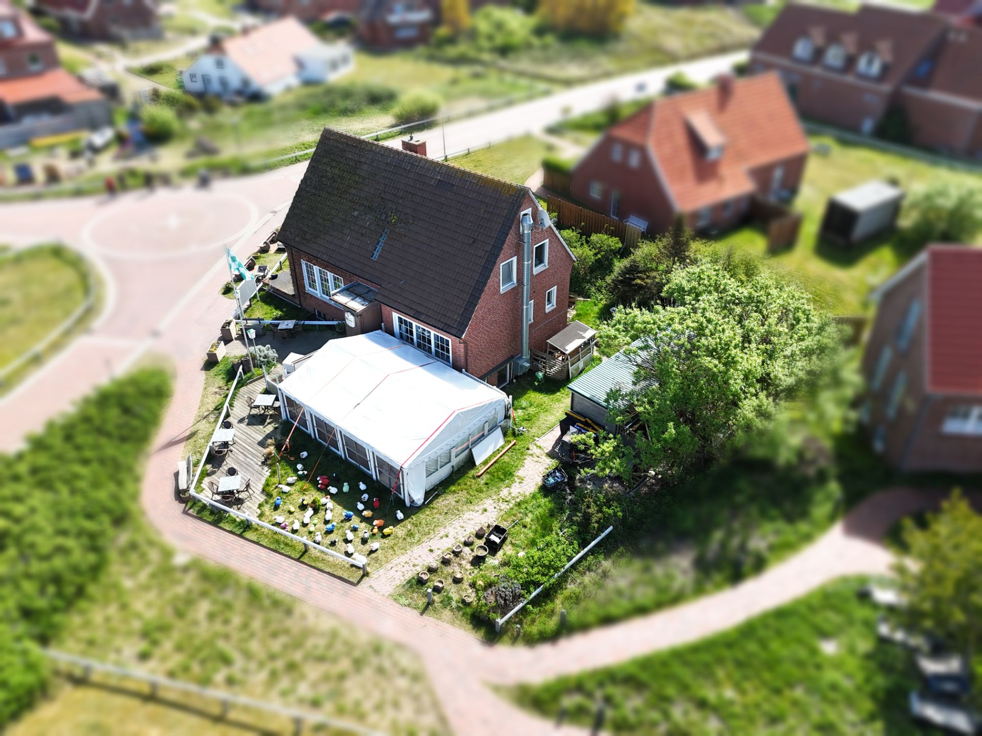 Backstein-Einfamilienhaus mit Garten, großem Zelt und Blumenbeeten, aus der Vogelperspektive.