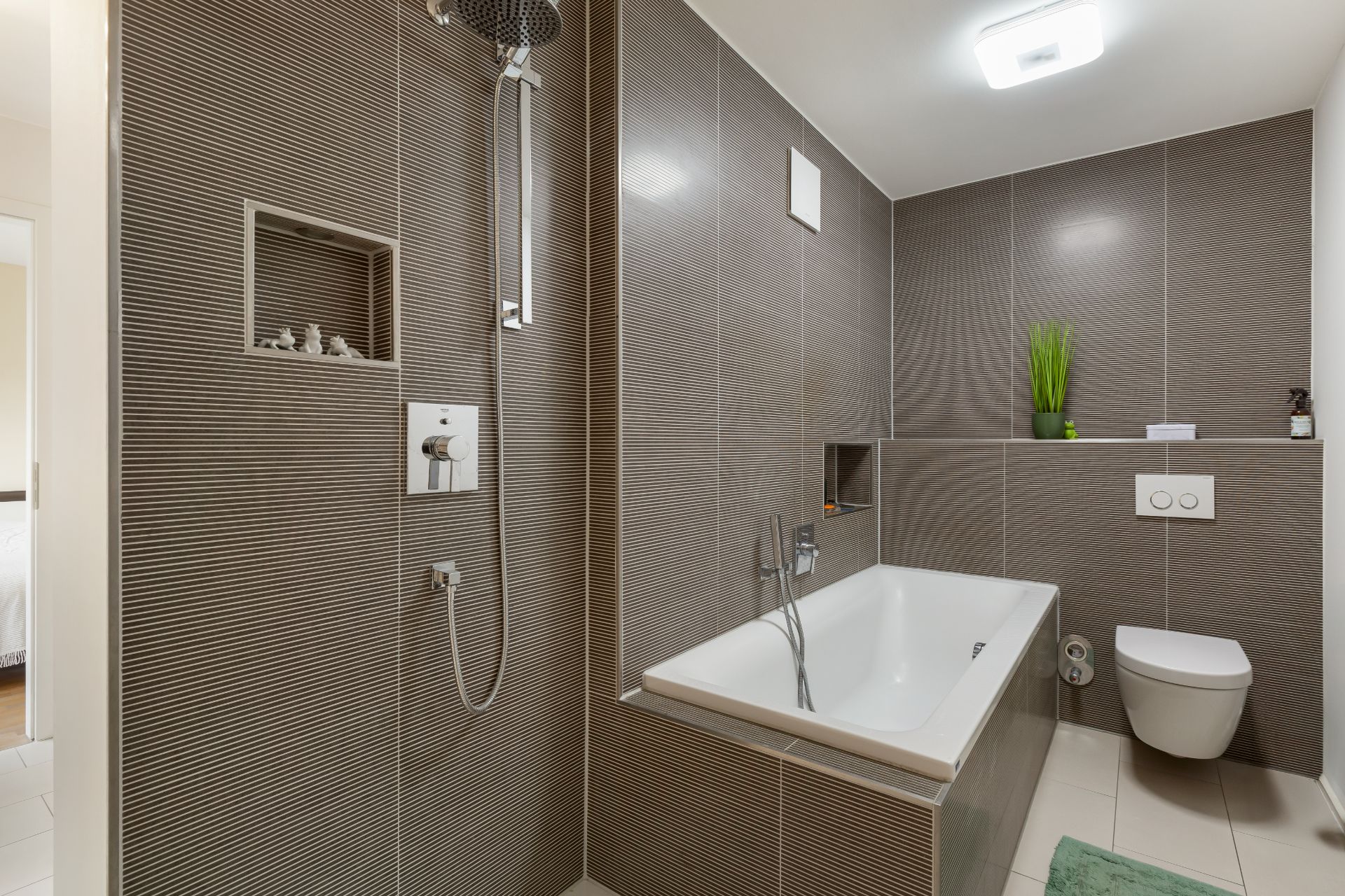 Modernes Badezimmer mit Badewanne, Dusche, Wandtoilette und grauen Fliesen.