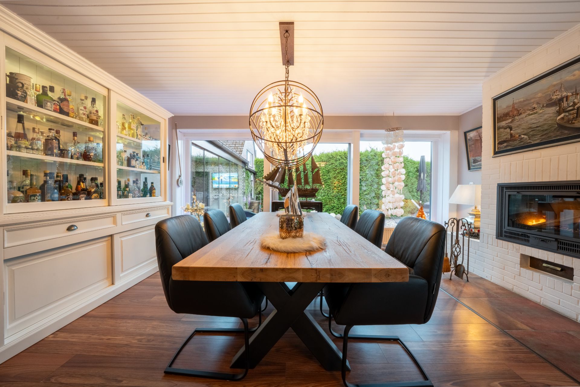 Esszimmer mit langem Holztisch, schwarzen Stühlen, Kamin und großem Getränkeschrank.