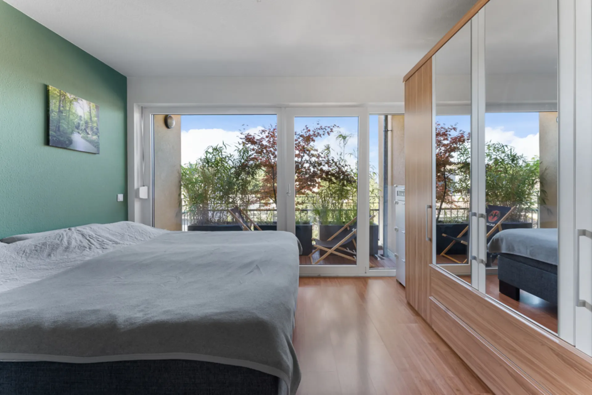 Helles Schlafzimmer mit Doppelbett, Spiegelschrank und Zugang zu einem Balkon mit Pflanzen.