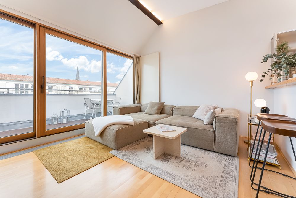 Helles Wohnzimmer mit Ecksofa, Couchtisch und großem Fenster zur Terrasse.