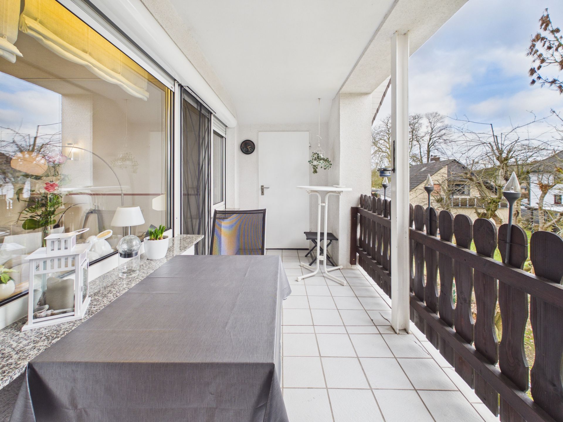 Überdachter Balkon mit Tisch, Stuhl, Deko und Blick auf Nachbarhäuser.