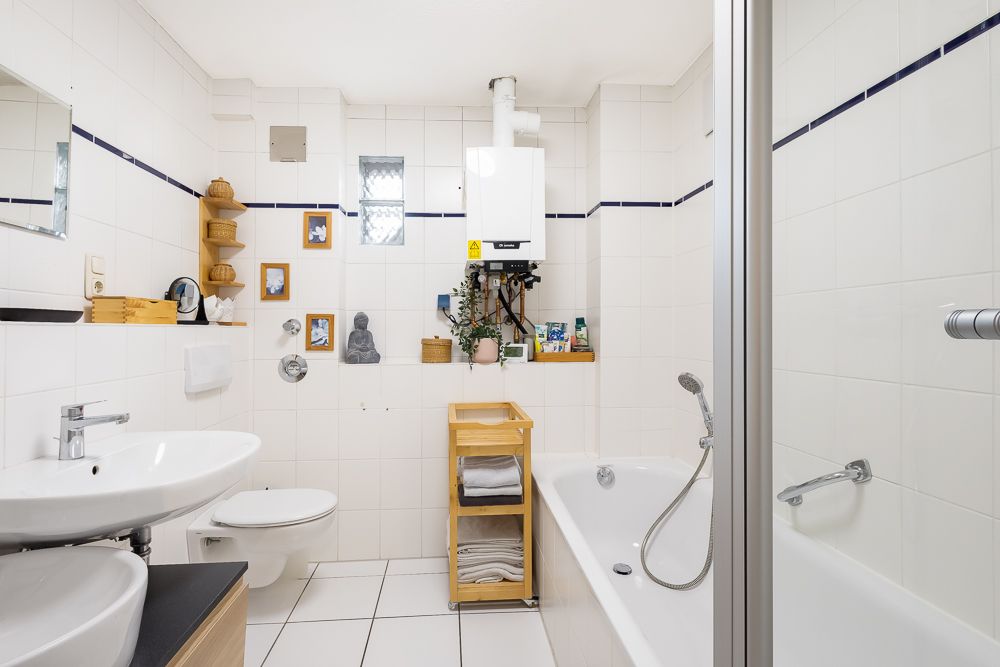 Helles Badezimmer mit Badewanne, Waschbecken, WC und Regalen an der gefliesten Wand.
