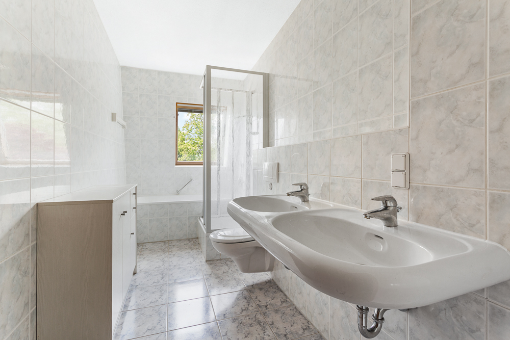 Helles Badezimmer mit zwei Waschbecken, Duschkabine, WC, Badewanne und Fenster.