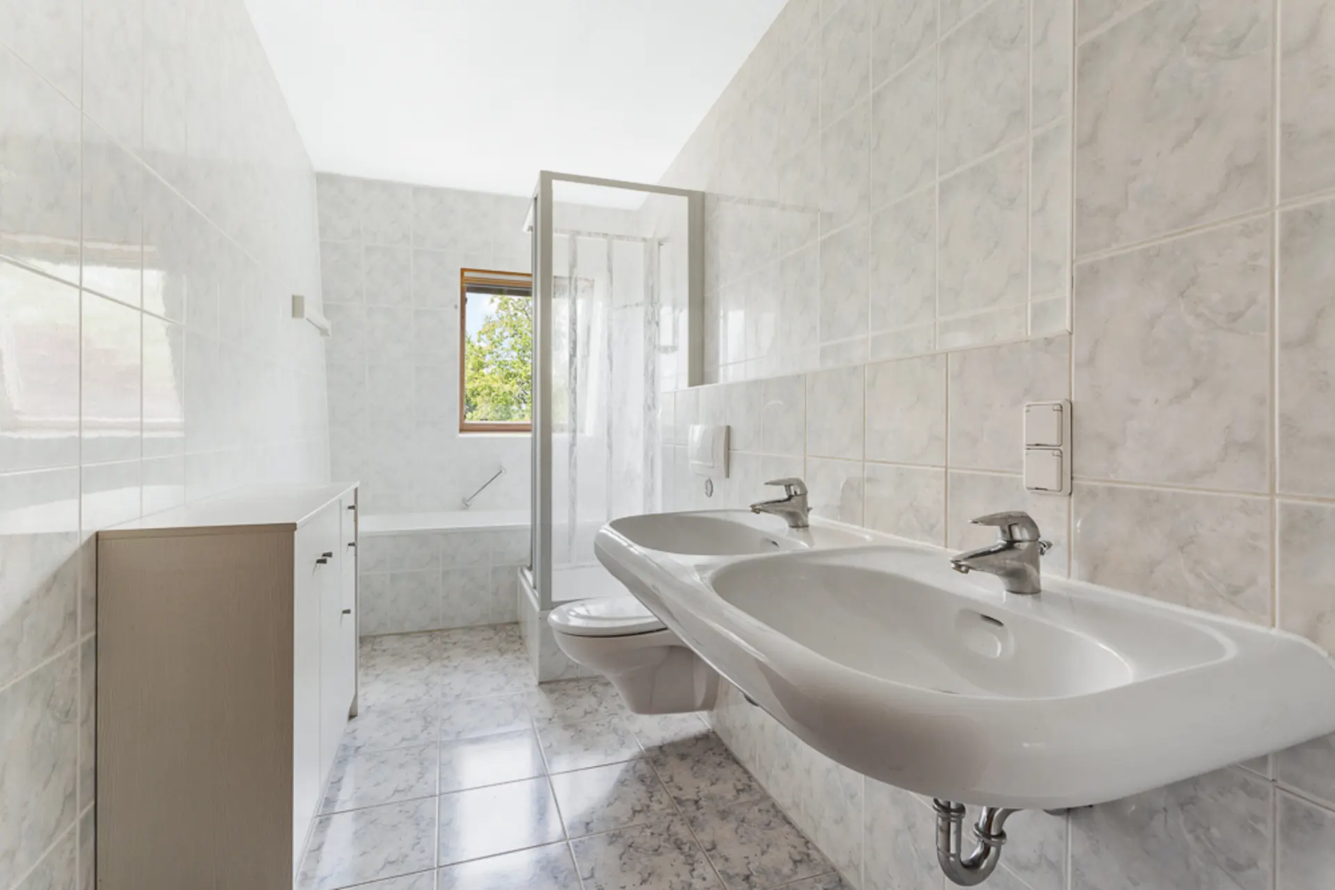 Helles Badezimmer mit zwei Waschbecken, Duschkabine, WC, Badewanne und Fenster.