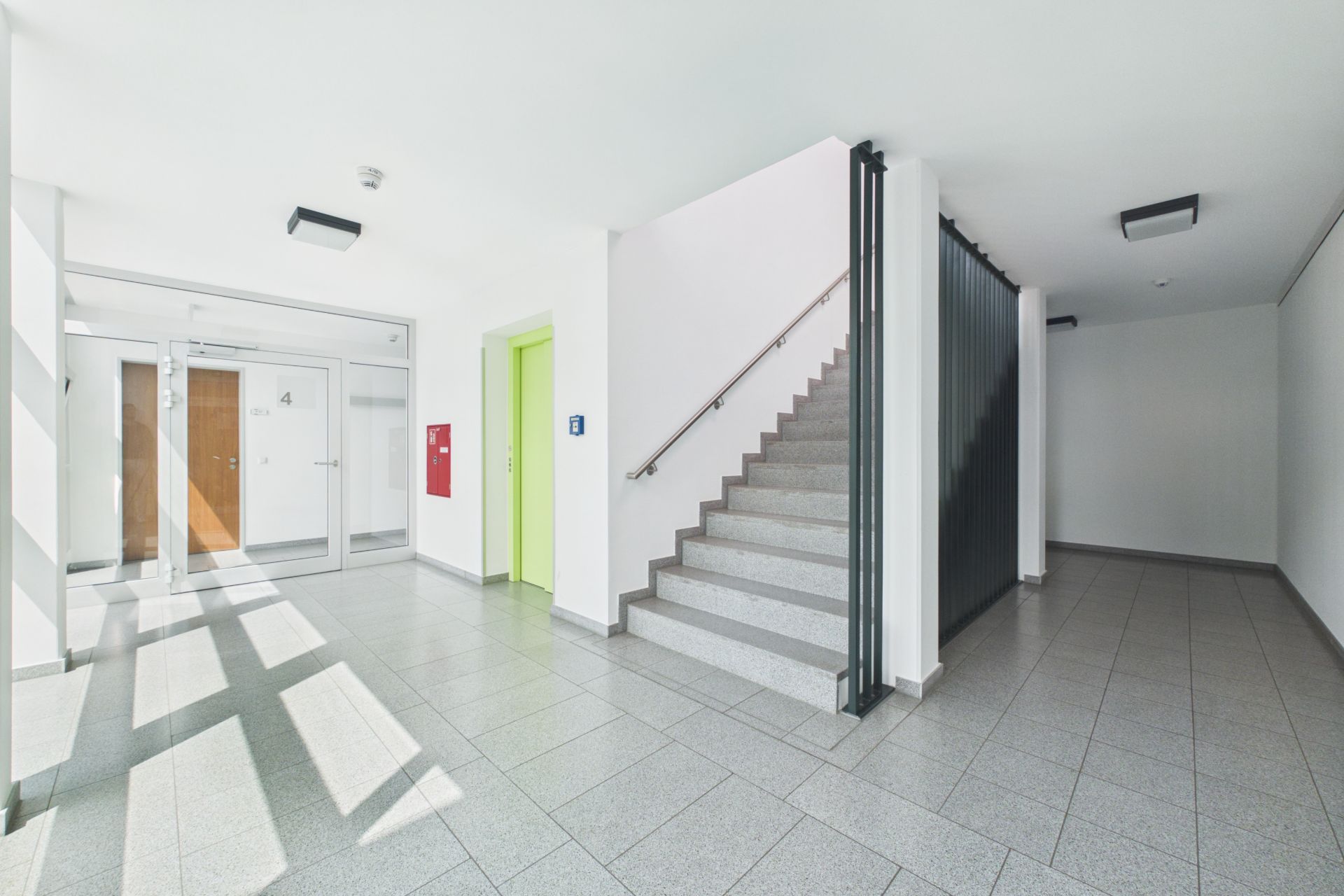Heller Eingangsbereich mit Treppe, Aufzug mit grüner Tür und Flur in einem Wohnhaus.