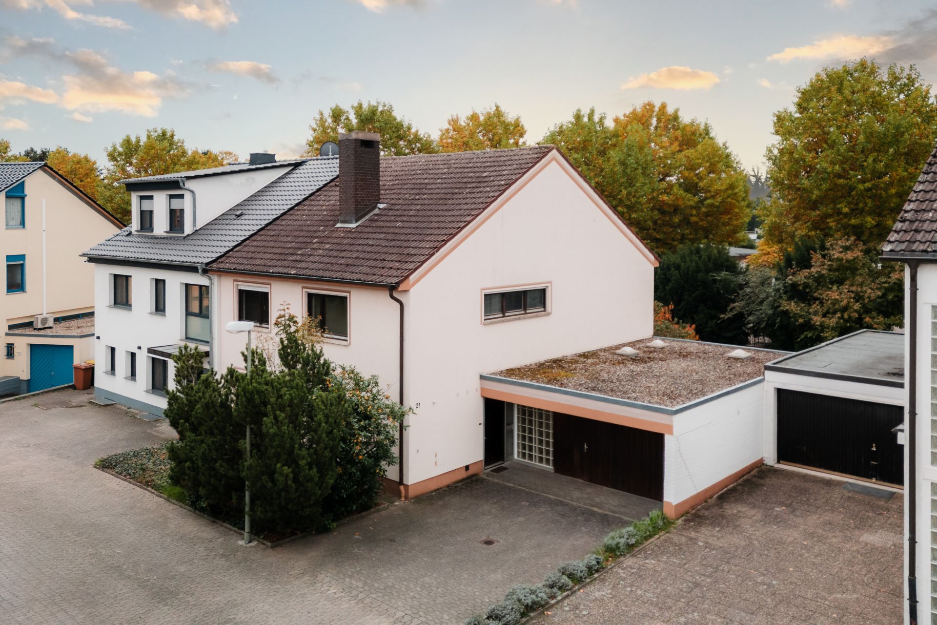 Zweistöckiges Wohnhaus mit Garage, umgeben von Bäumen und einem gepflasterten Hof.