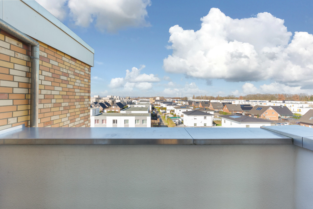 Blick von einem Balkon auf ein Wohngebiet mit Häusern unter blauem Himmel und Wolken.