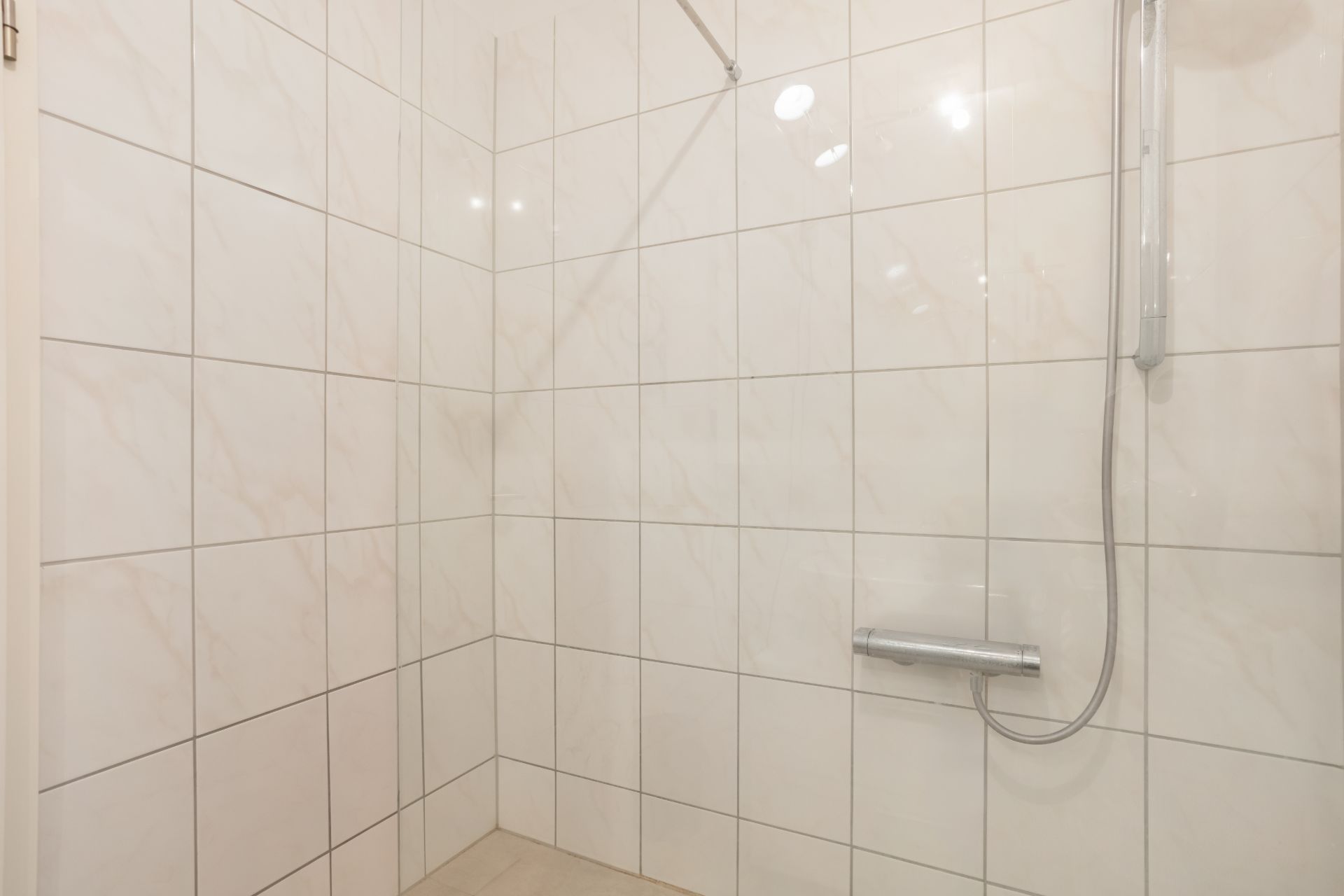 Begehbare Dusche mit weißen Fliesen und silberner Duscharmatur.