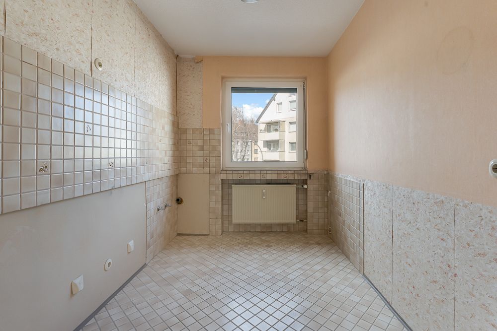 Leerer Raum mit gefliesten Wänden und Boden, Fenster mit Blick auf Wohngebäude.