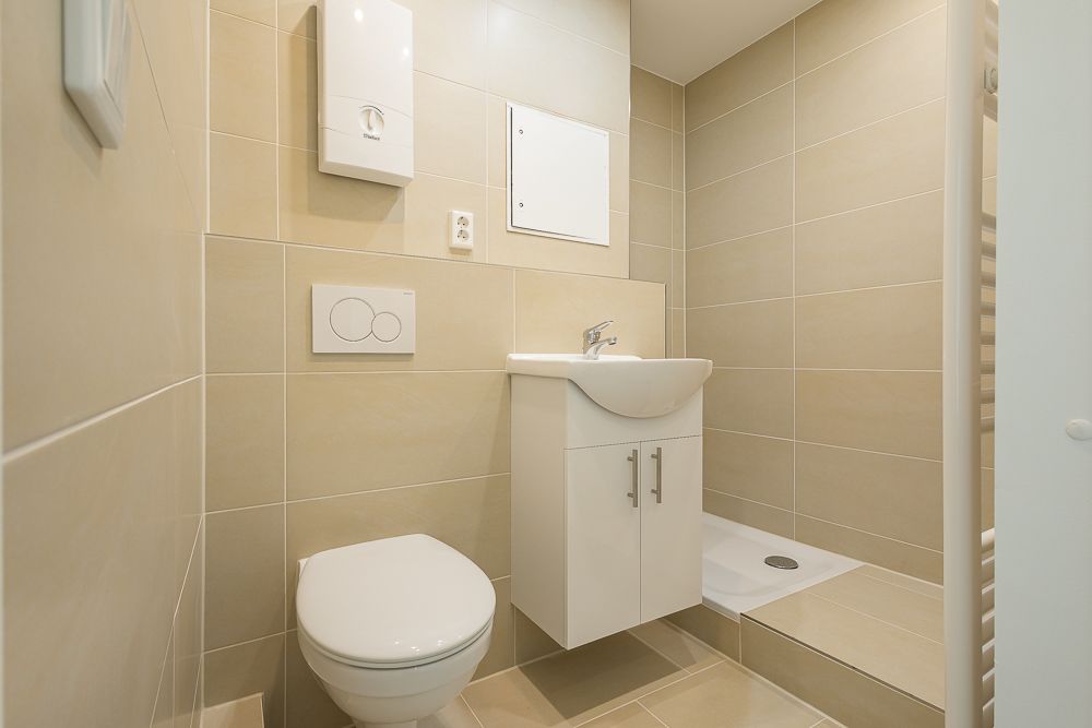 Modernes Badezimmer mit Toilette, Waschbecken und offener Dusche, beige Fliesen an Wänden und Boden.