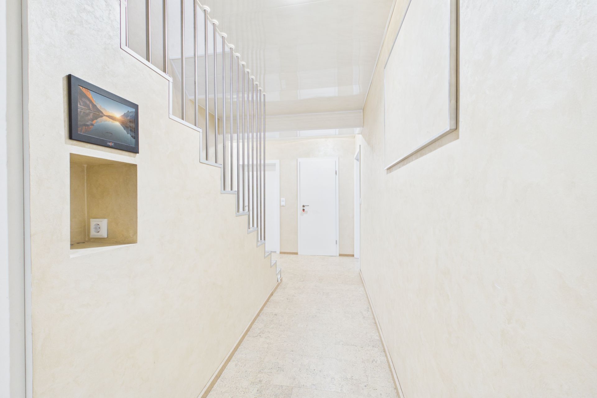 Heller Flur mit Treppe, weißer Tür und Bild an der Wand.