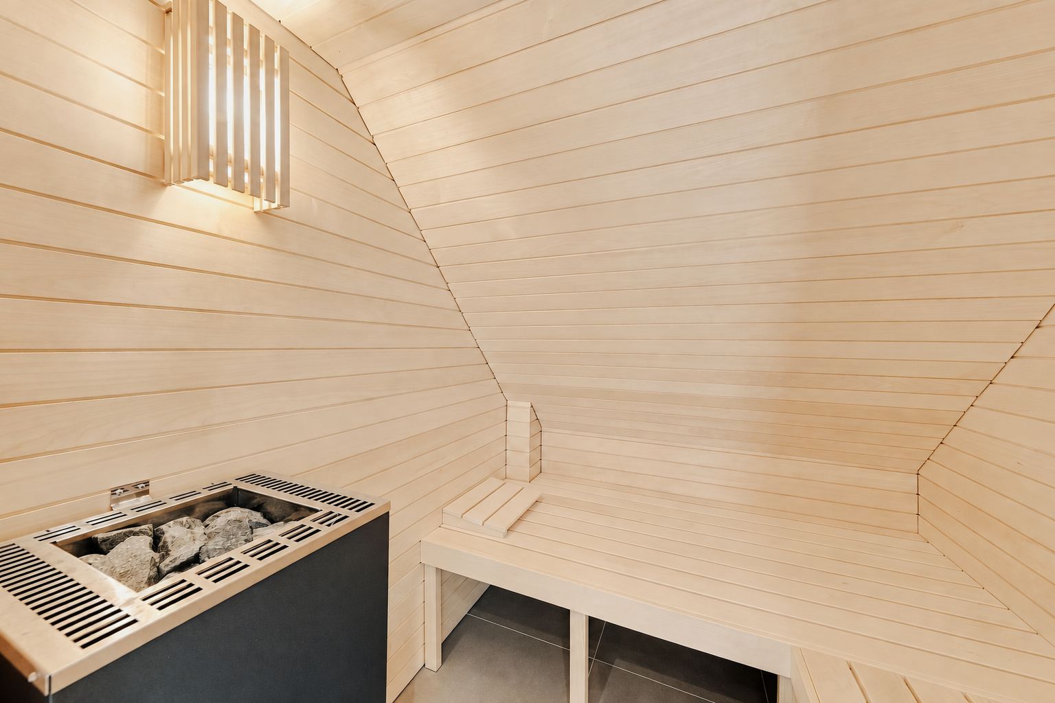 Helle Holzsauna mit Bank, Ofen und Wandlampe sichtbar.