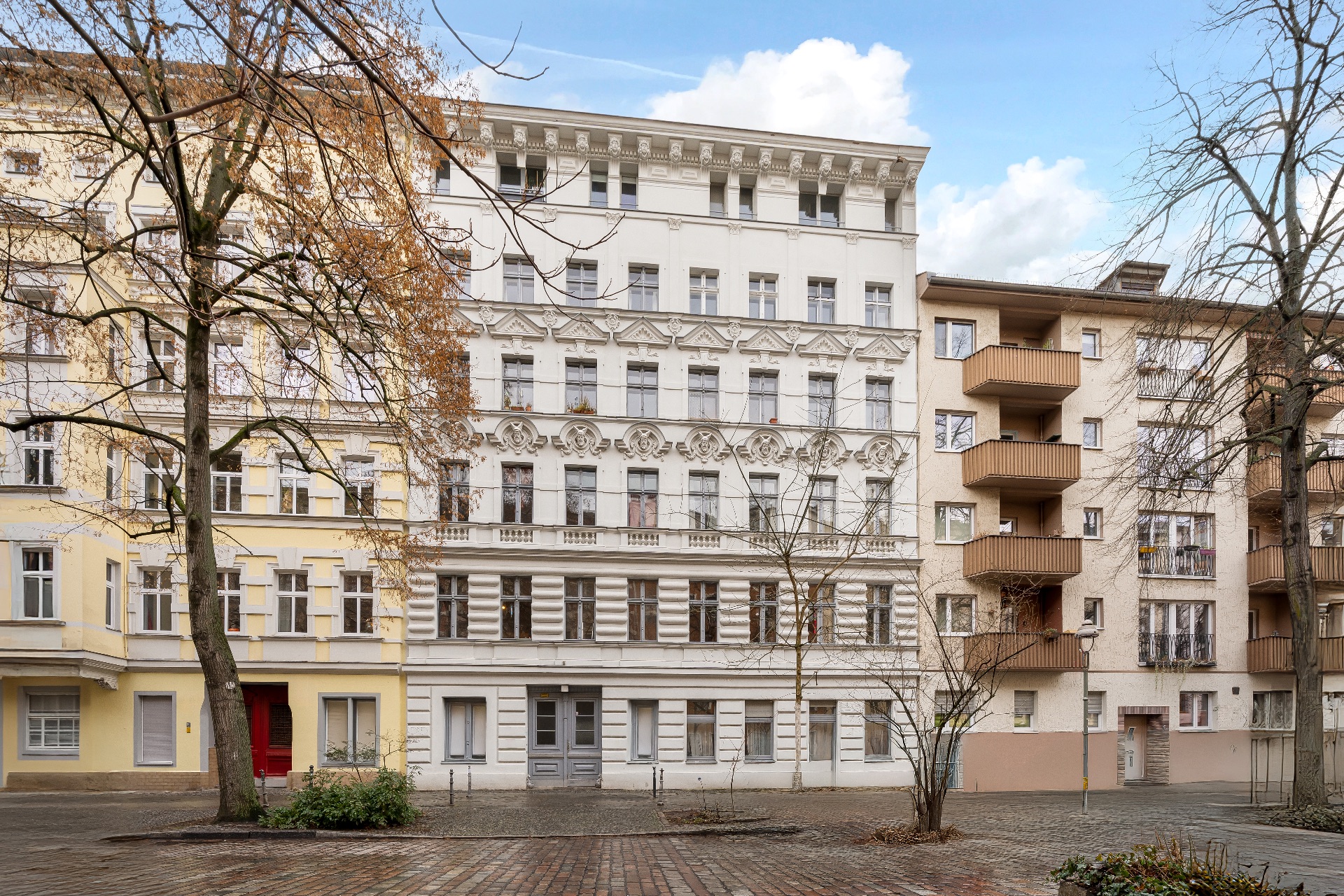 Mehrstöckiges Wohnhaus mit verzierten Fassaden und mehreren Fenstern, Bäume im Vordergrund.