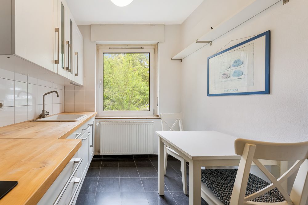 Helle Küche mit Holzarbeitsplatte, Fenster, kleinem Tisch und zwei Stühlen.