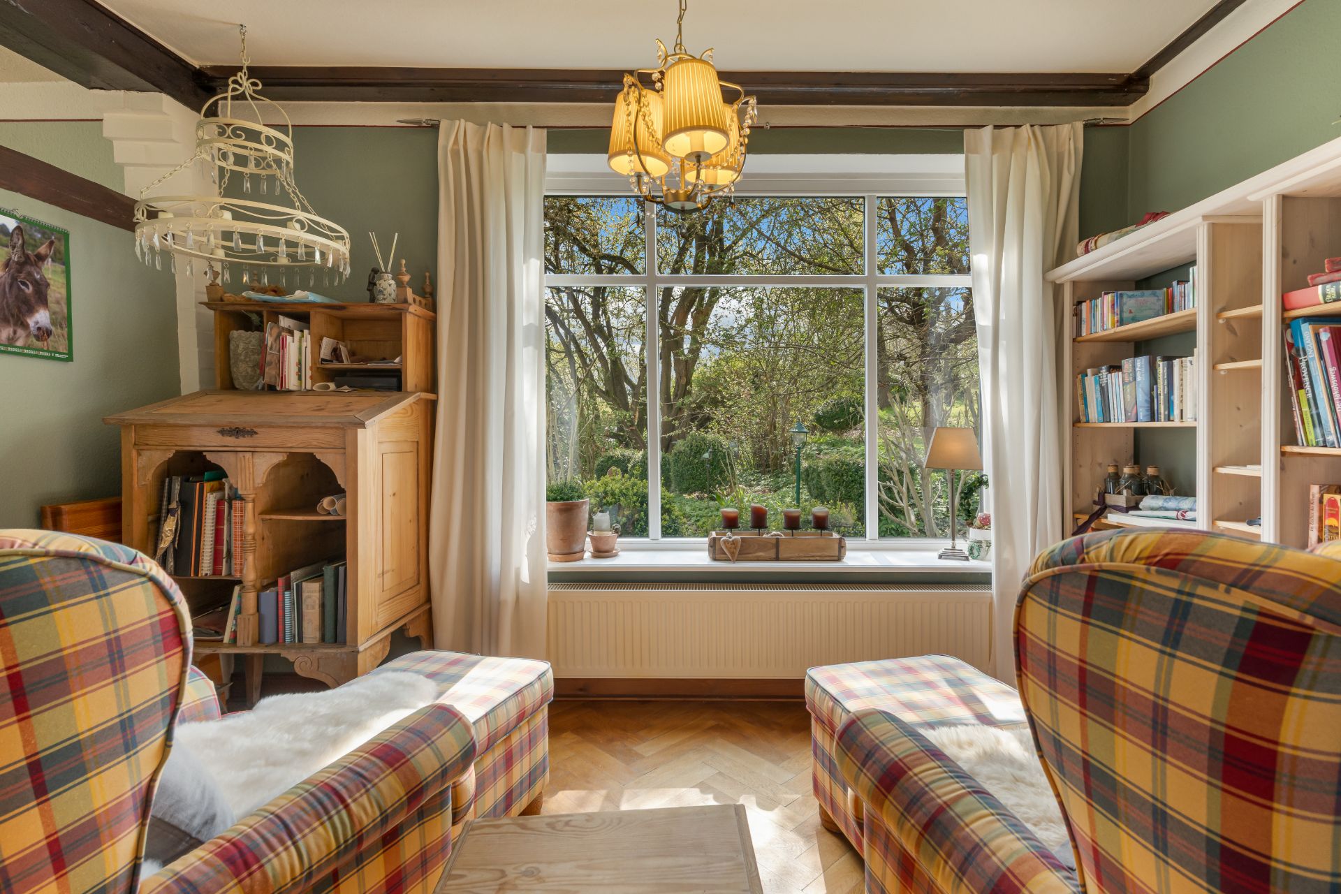 Gemütliches Wohnzimmer mit karierten Sesseln, Bücherregalen und großem Fenster mit Blick ins Grüne.