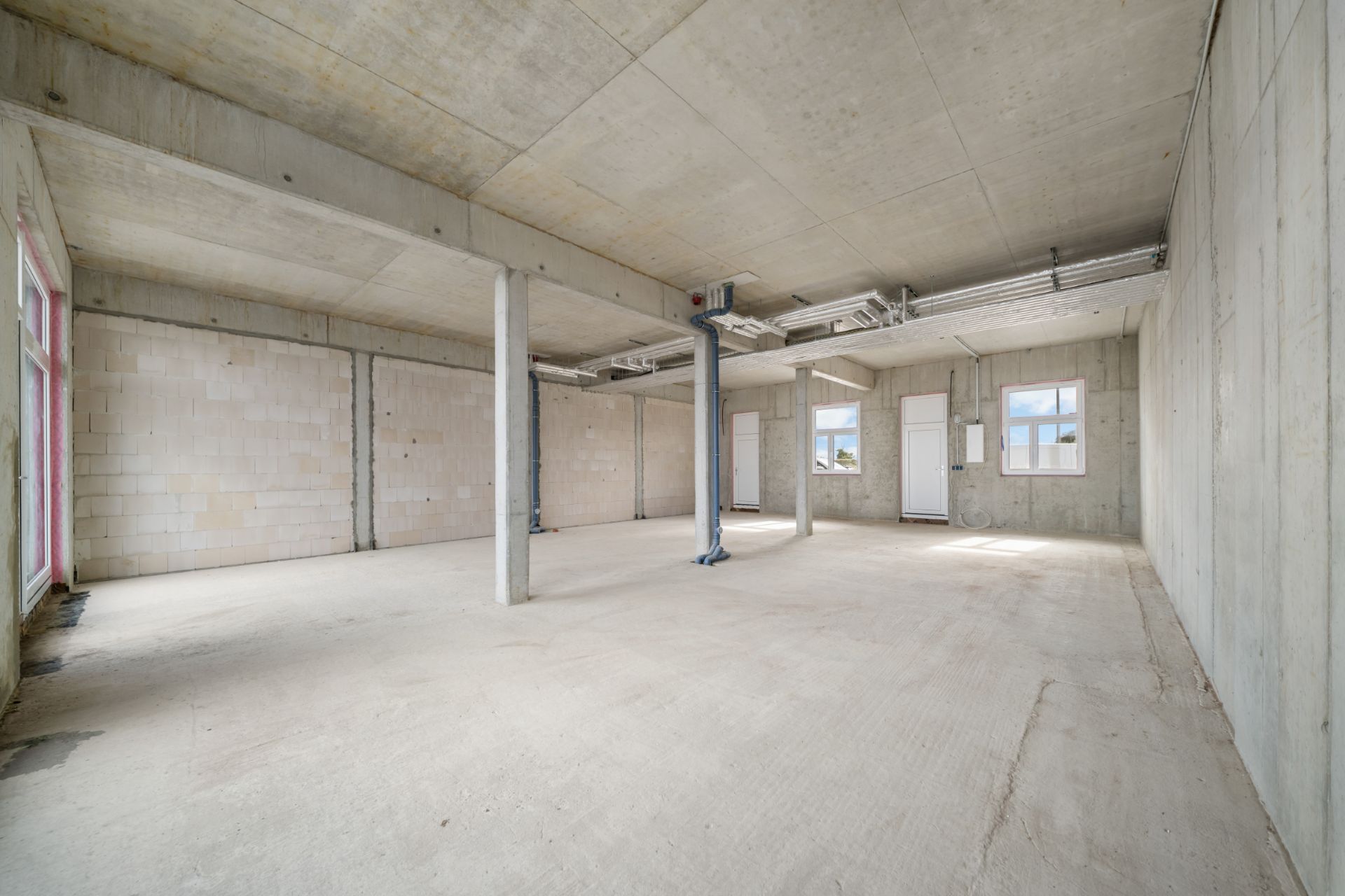 Leerer Raum mit Betonwänden, -boden und -decke sowie mehreren Fenstern und Säulen.