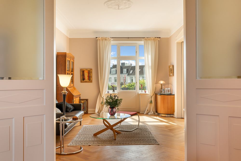 Helles Wohnzimmer mit großem Fenster, Sofa, Glastisch, Teppich und Holzmöbeln.