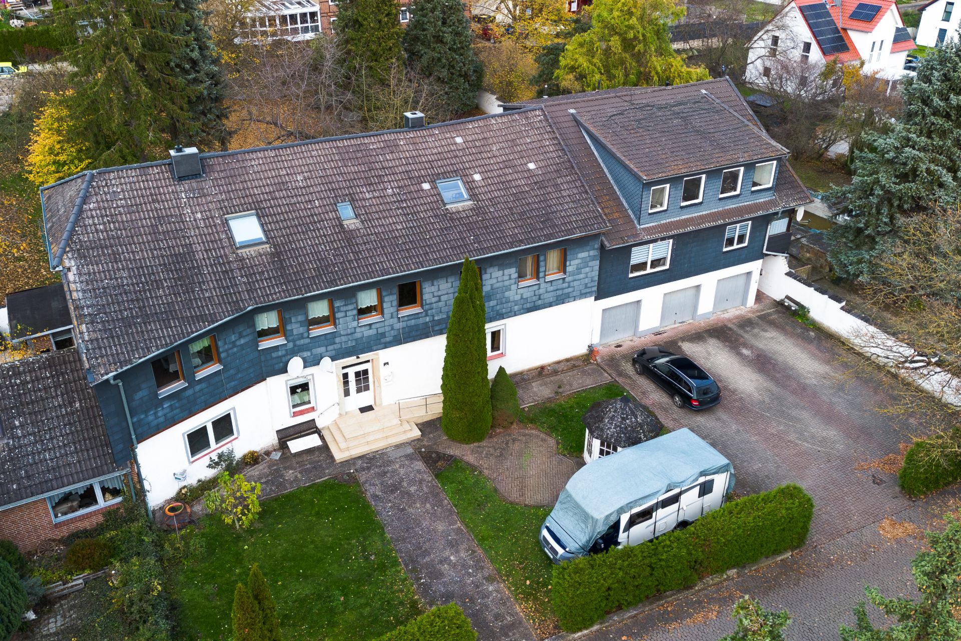 Großes Wohnhaus mit mehreren Eingängen, Garagen, geparktem Auto und Wohnmobil vor dem Haus.