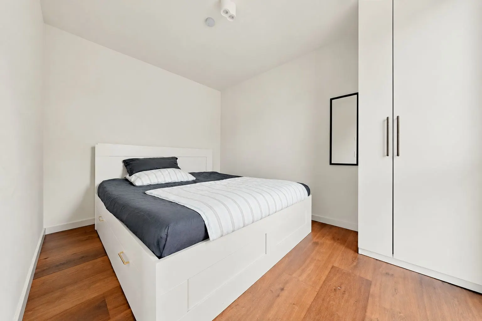 Schlafzimmer mit Doppelbett, weißem Kleiderschrank und Holzfußboden.