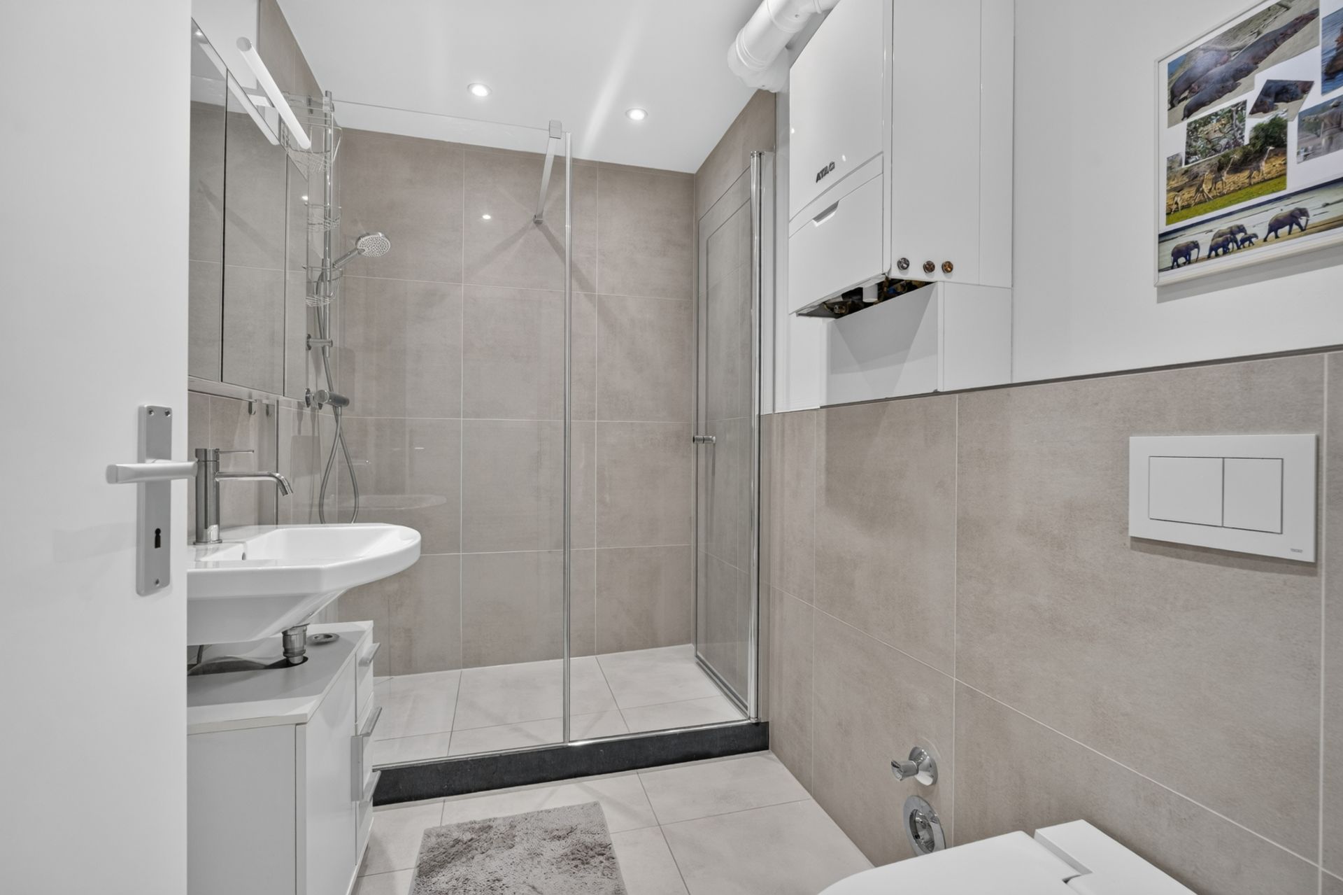 Modernes Badezimmer mit ebenerdiger Dusche, Waschbecken und WC, hellen Fliesen und weißen Möbeln.