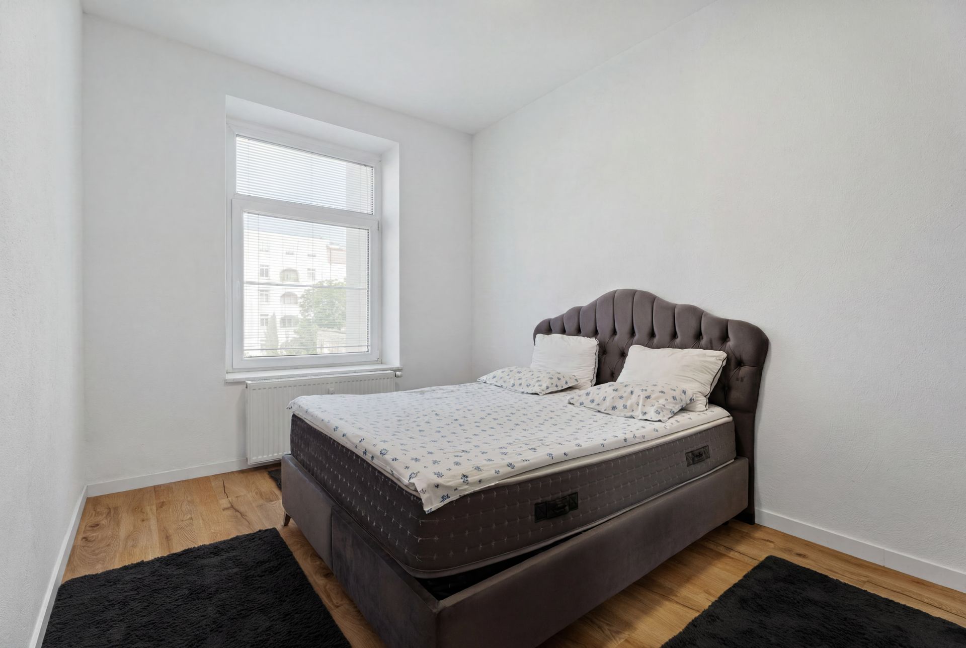 Schlafzimmer mit Doppelbett, zwei Kissen, Holzboden und großem Fenster.