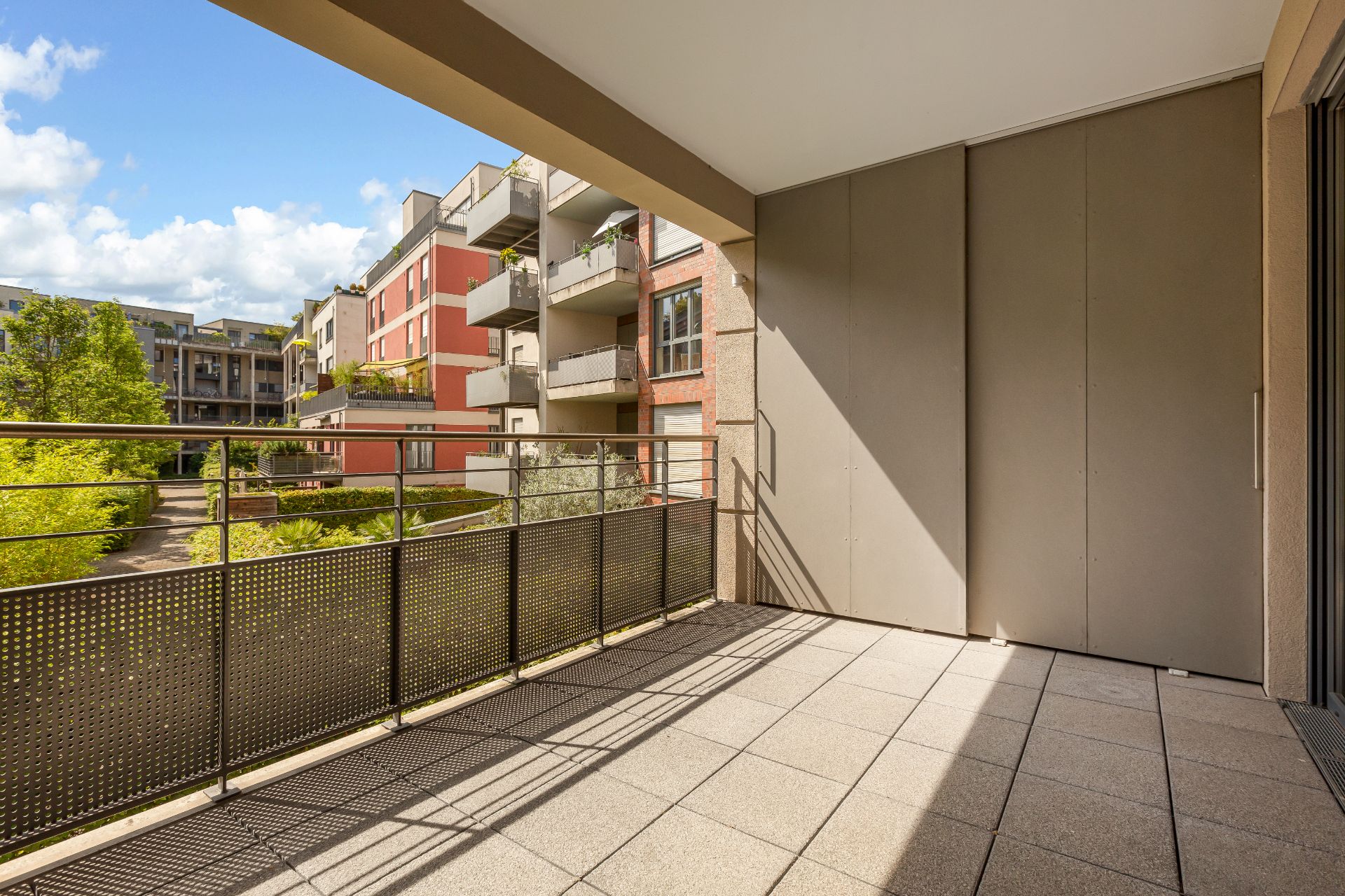 Großer Balkon mit Metallgeländer, Blick auf begrünte Wohnanlage und Nachbargebäude.