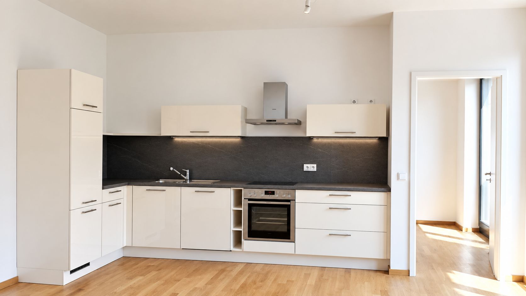 Helle Einbauküche mit Backofen, Spüle und weißen Schränken auf Parkettboden.