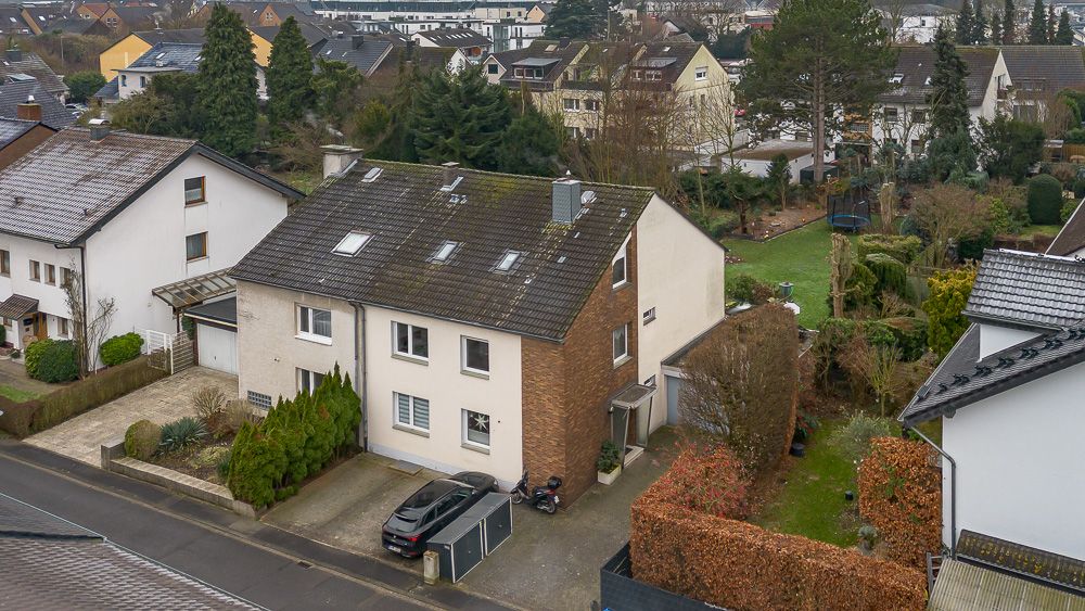 Zweistöckiges Wohnhaus mit Einfahrt, Auto und umliegenden Gärten in einem Wohngebiet.