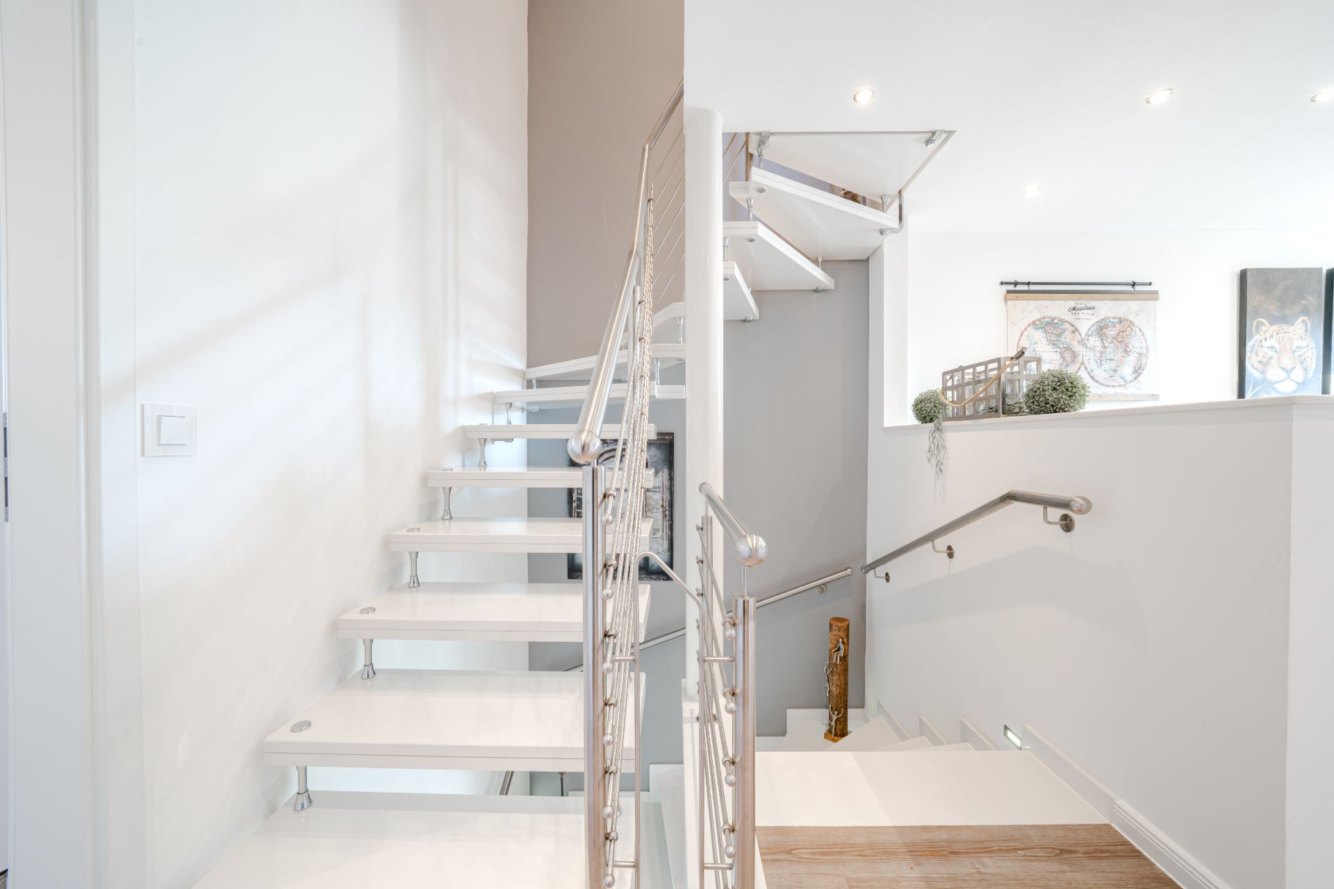 Moderne weiße Treppe mit Metallgeländer in einem hellen Wohnraum.