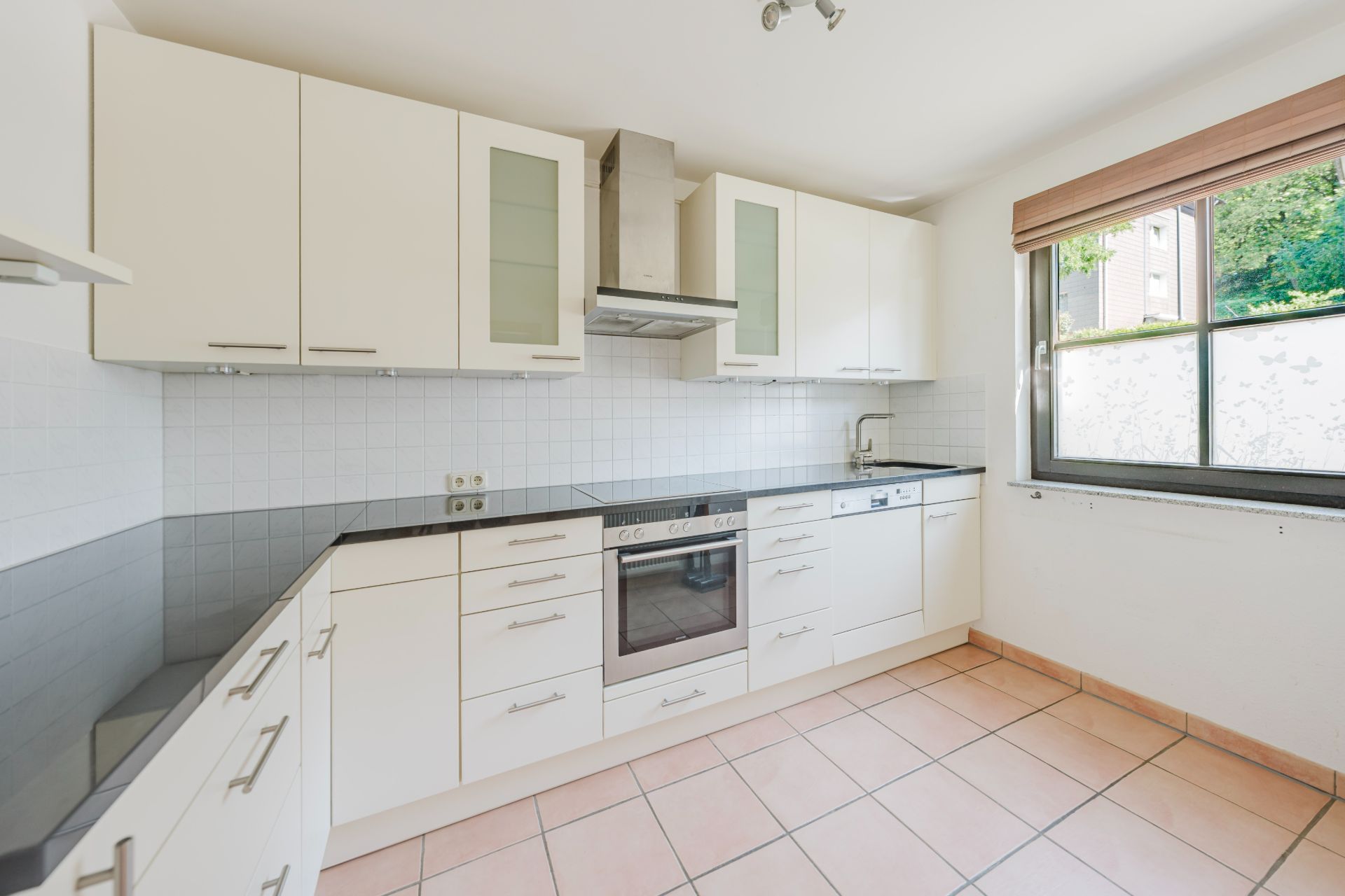 Moderne Einbauküche mit weißen Schränken, Herd, Spüle und großem Fenster.