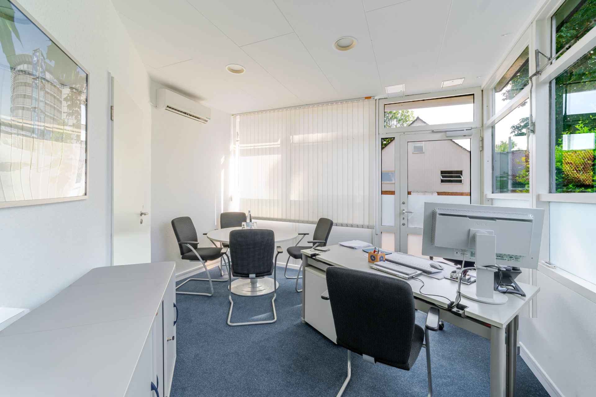Helles Arbeitszimmer mit Schreibtisch, Stühlen und großem Fenster.