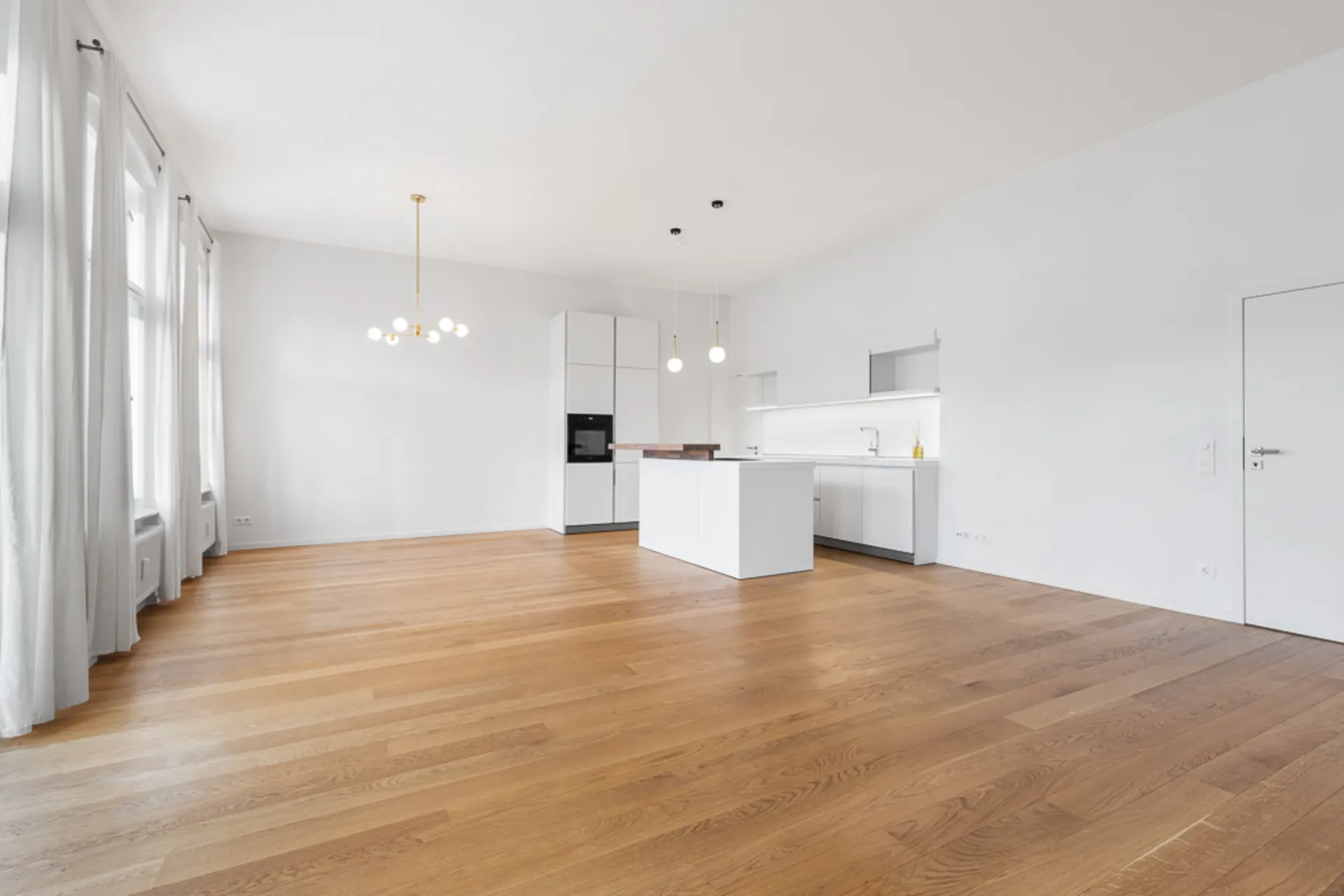 Helles, modernes Wohnzimmer mit offener Küche, Holzboden und großen Fenstern mit weißen Vorhängen.