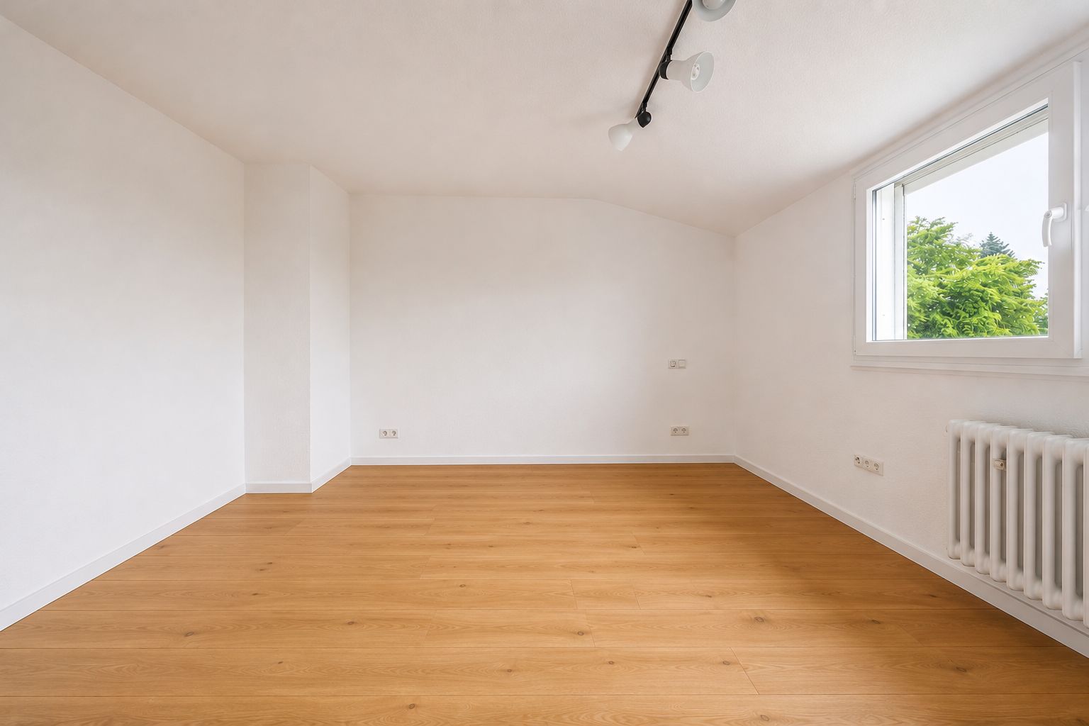 Leerer Raum mit weiß gestrichenen Wänden, Holzfußboden, Fenster und Heizkörper.