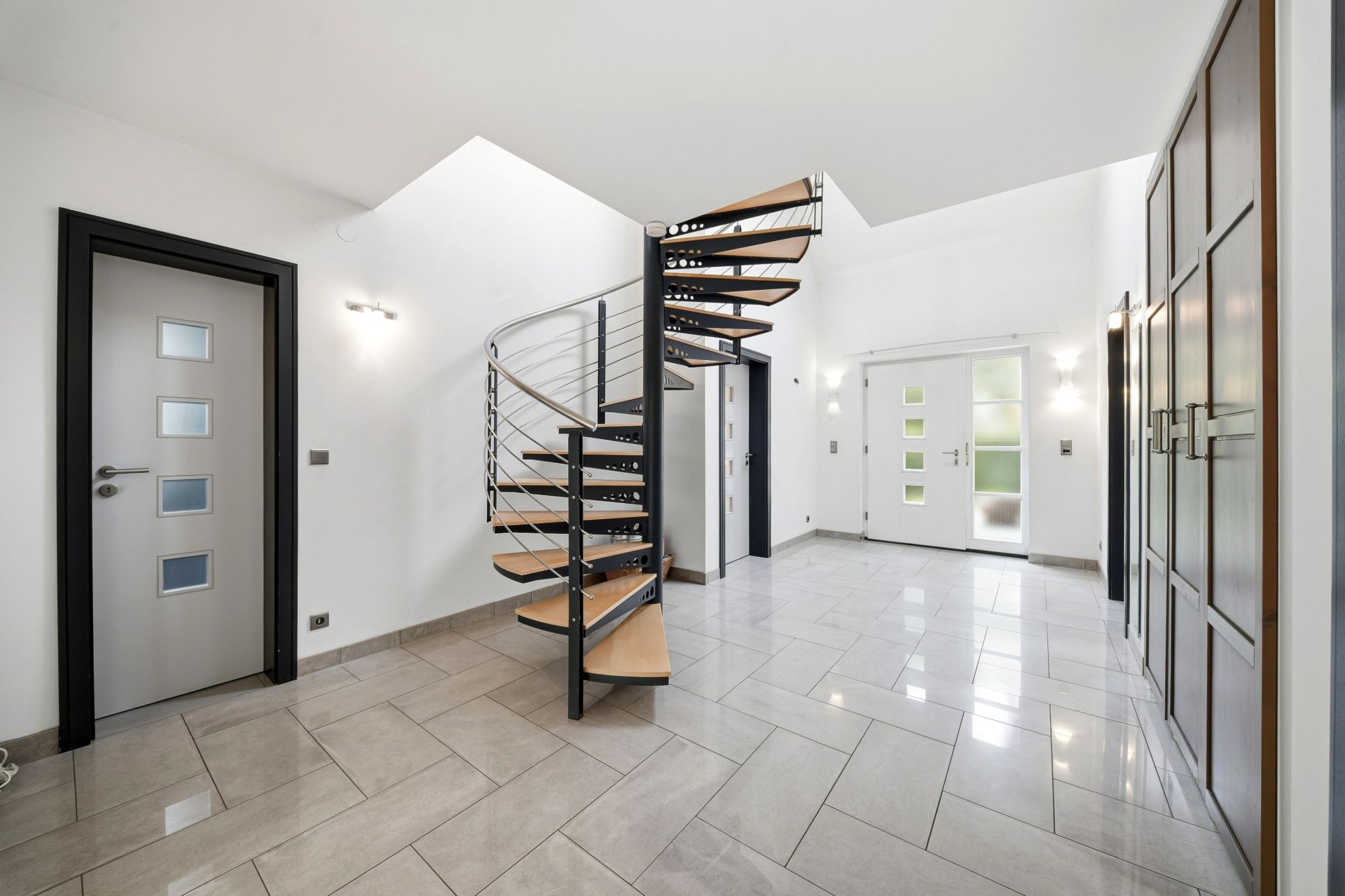 Heller Flur mit Wendeltreppe, Fliesenboden, Türen und Einbauschränken.