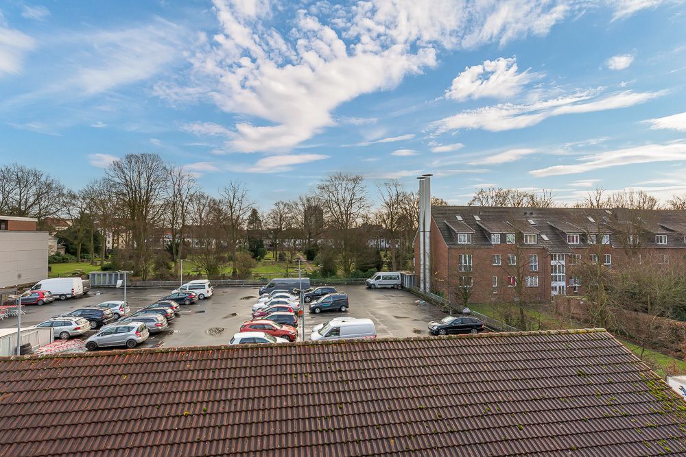 Blick auf einen Parkplatz mit Autos, Bäumen und Wohngebäuden im Hintergrund.