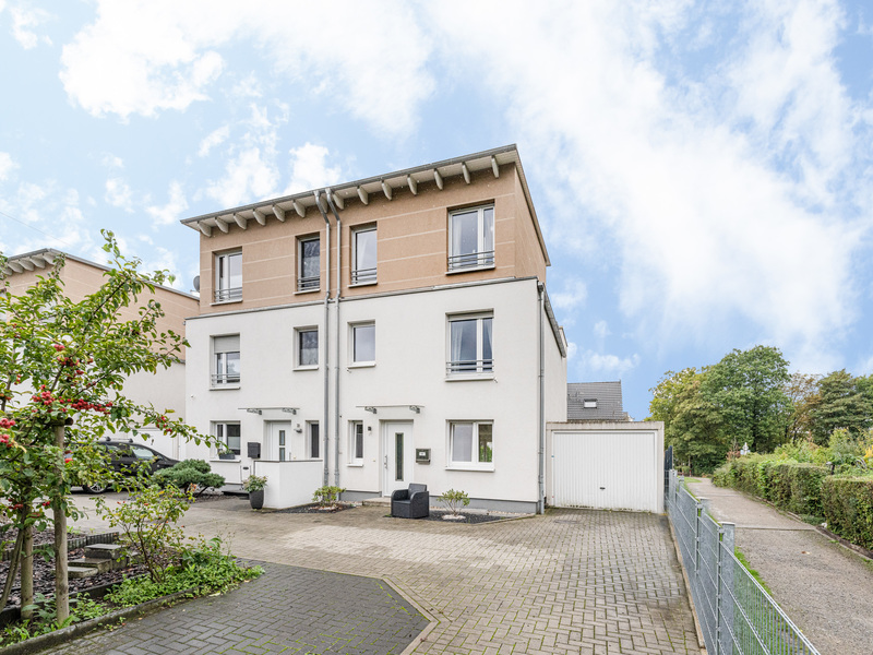 Modernes, dreistöckiges Doppelhaus mit weißer Fassade und gepflastertem Vorhof.