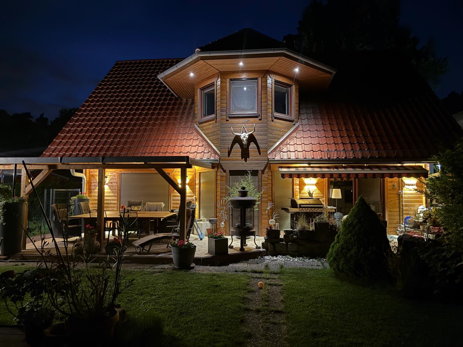 Ein beleuchtetes Einfamilienhaus mit überdachter Terrasse und Garten bei Nacht.