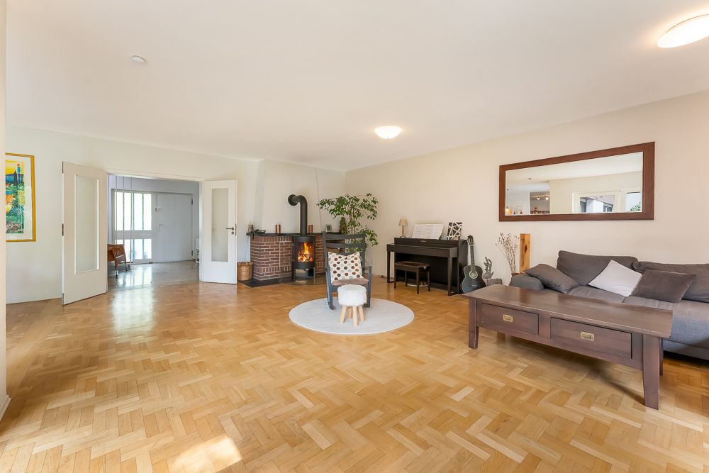 Helles Wohnzimmer mit Parkettboden, Sofa, Kamin, Klavier und großem Spiegel an der Wand.
