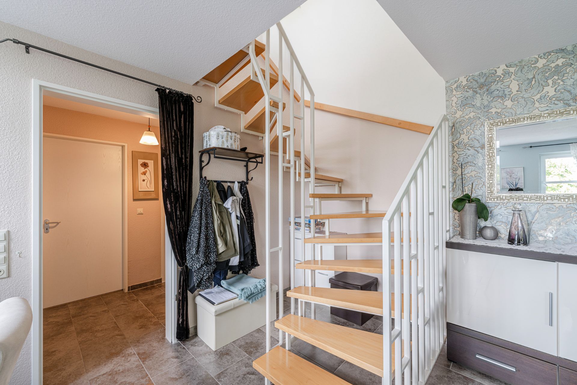 Heller Flur mit Holztreppe, Garderobe, Spiegel und Kommode mit Dekoration.