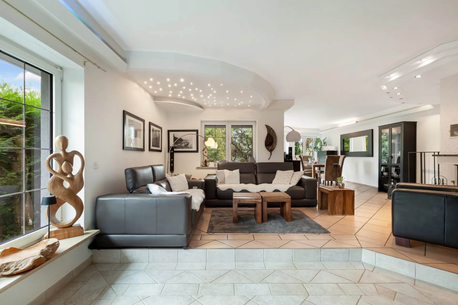 Modernes Wohnzimmer mit Ledersofas, Couchtischen und großen Fenstern, Blick auf Essbereich.