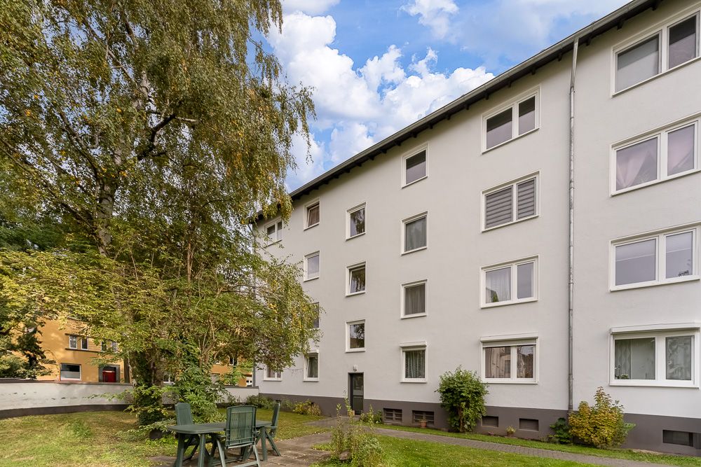 Mehrfamilienhaus mit weißer Fassade und Garten mit Sitzgruppe im Vordergrund.