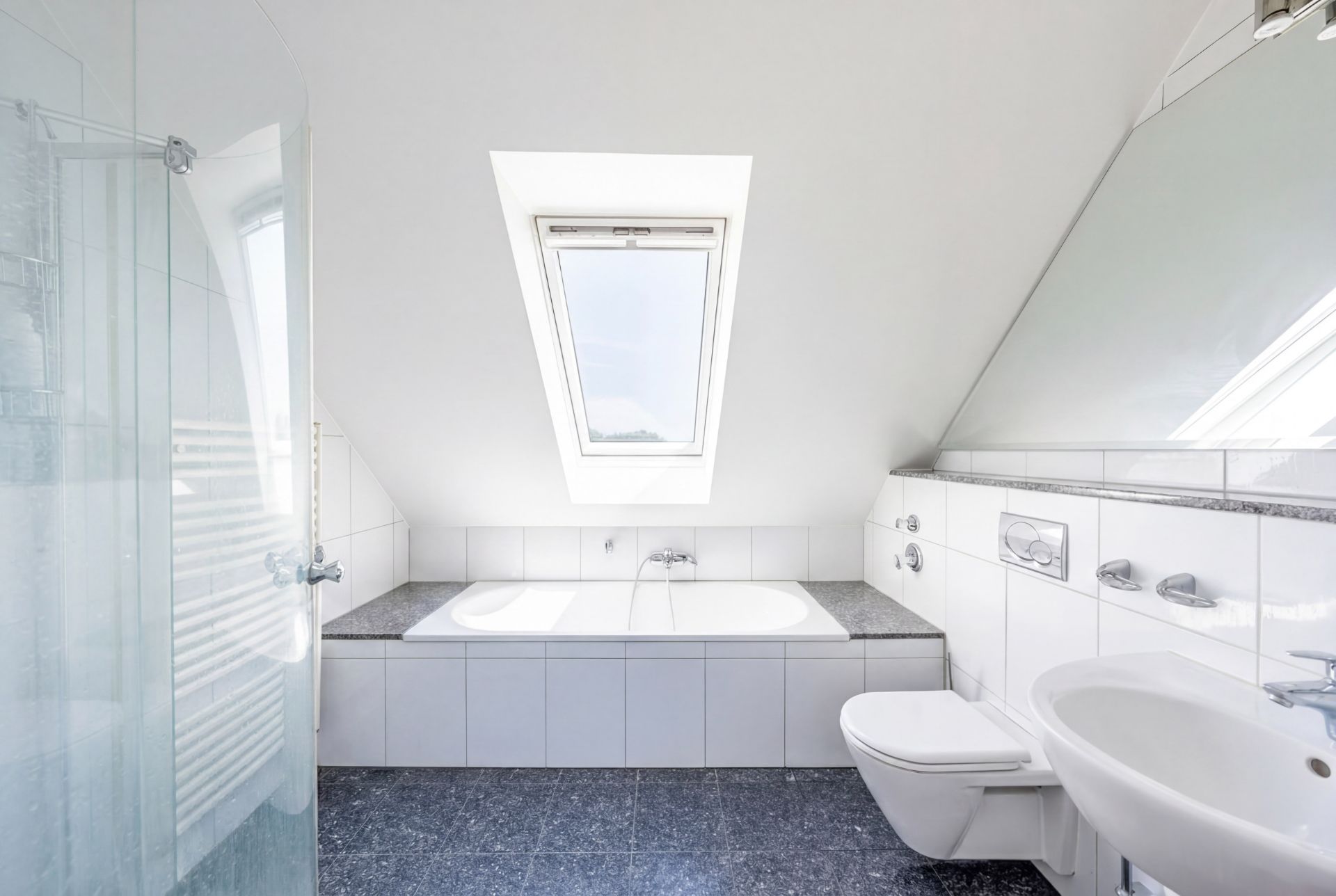 Helles Badezimmer mit Badewanne unter einem Dachfenster, WC, Waschbecken und Dusche.