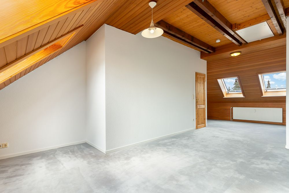 Helles Dachzimmer mit Holzdecke, Dachfenstern und Teppichboden.