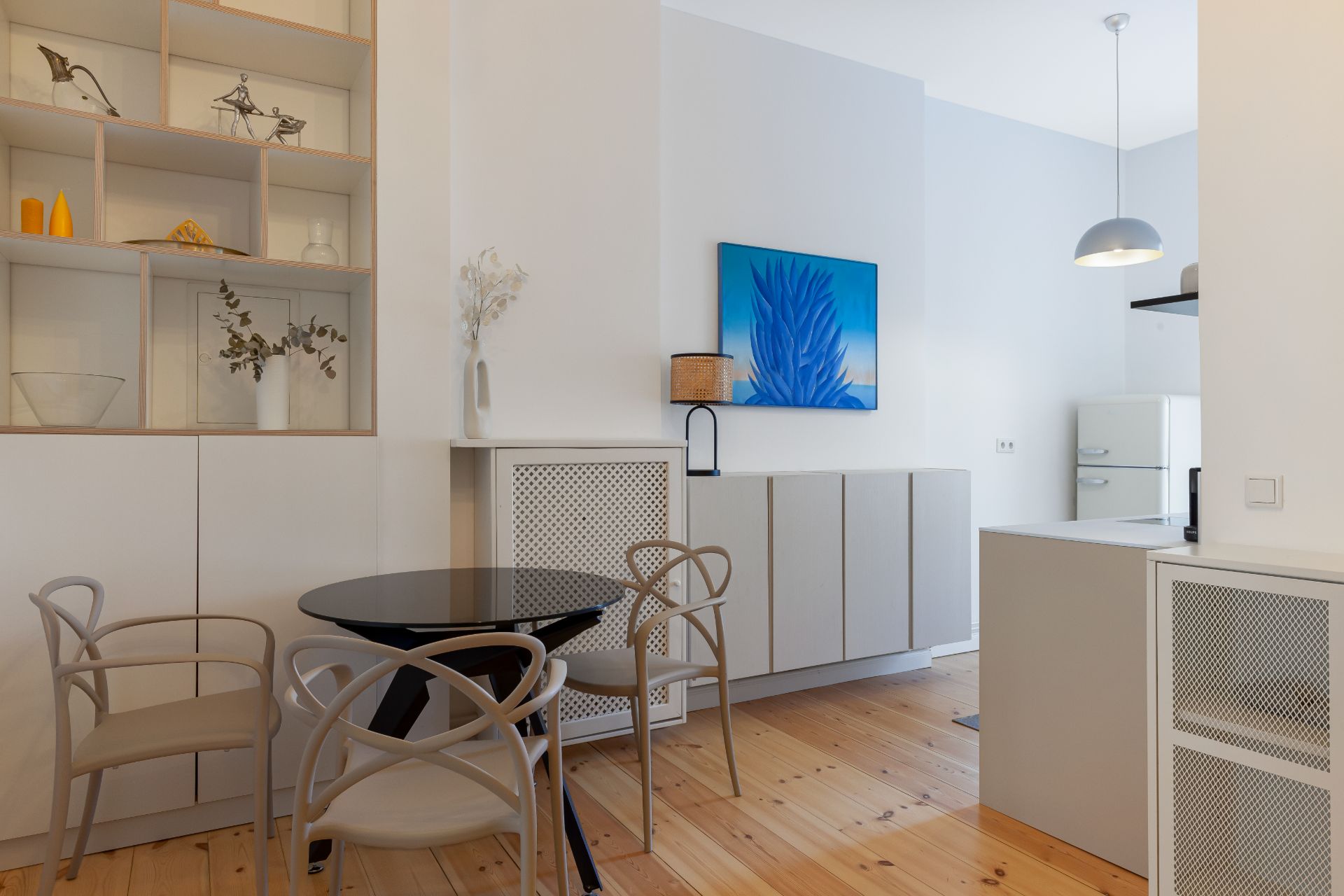 Helles Esszimmer mit rundem Tisch, vier Stühlen, Regal und moderner Küche im Hintergrund.