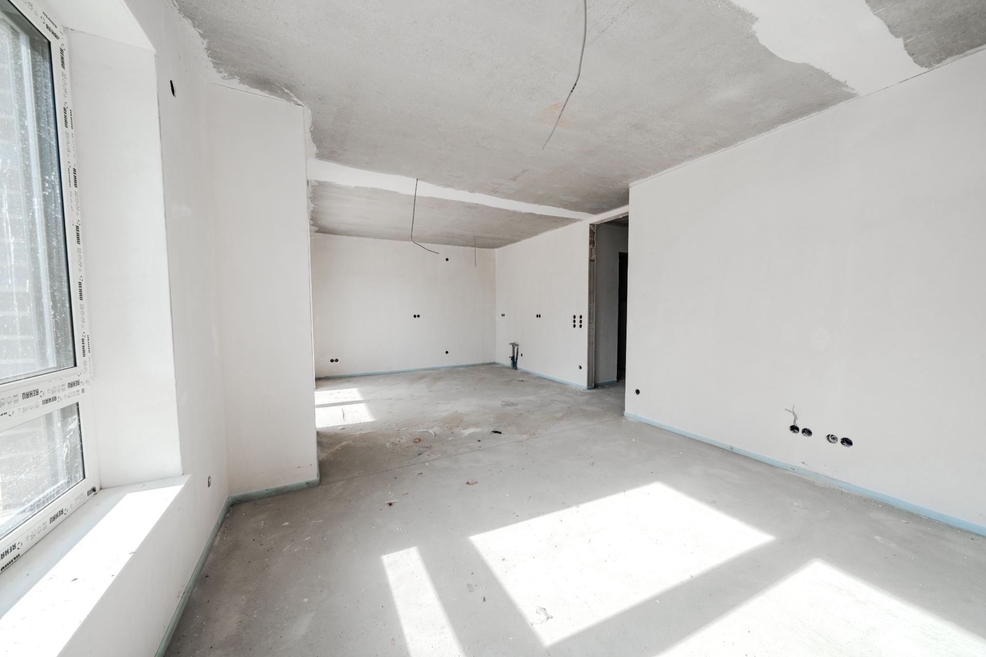 Heller leerer Raum mit großen Fenstern und unfertigen Wänden in einer Wohnung.
