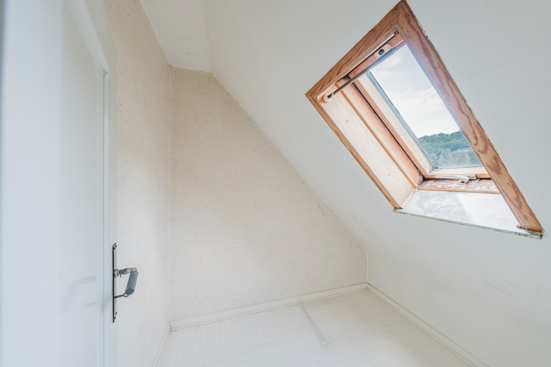 Kleiner leerer Raum mit Dachschräge und offenem Dachfenster.